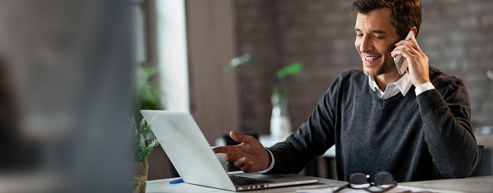 Smiling man on phone pointing at laptop